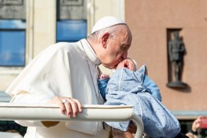 Pope Francis in healthier days, kissing baby during a visit to Estonia in 2018. © Creative Commons. 
